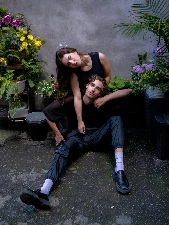 a couple poses for the camera in front of plants and flowers