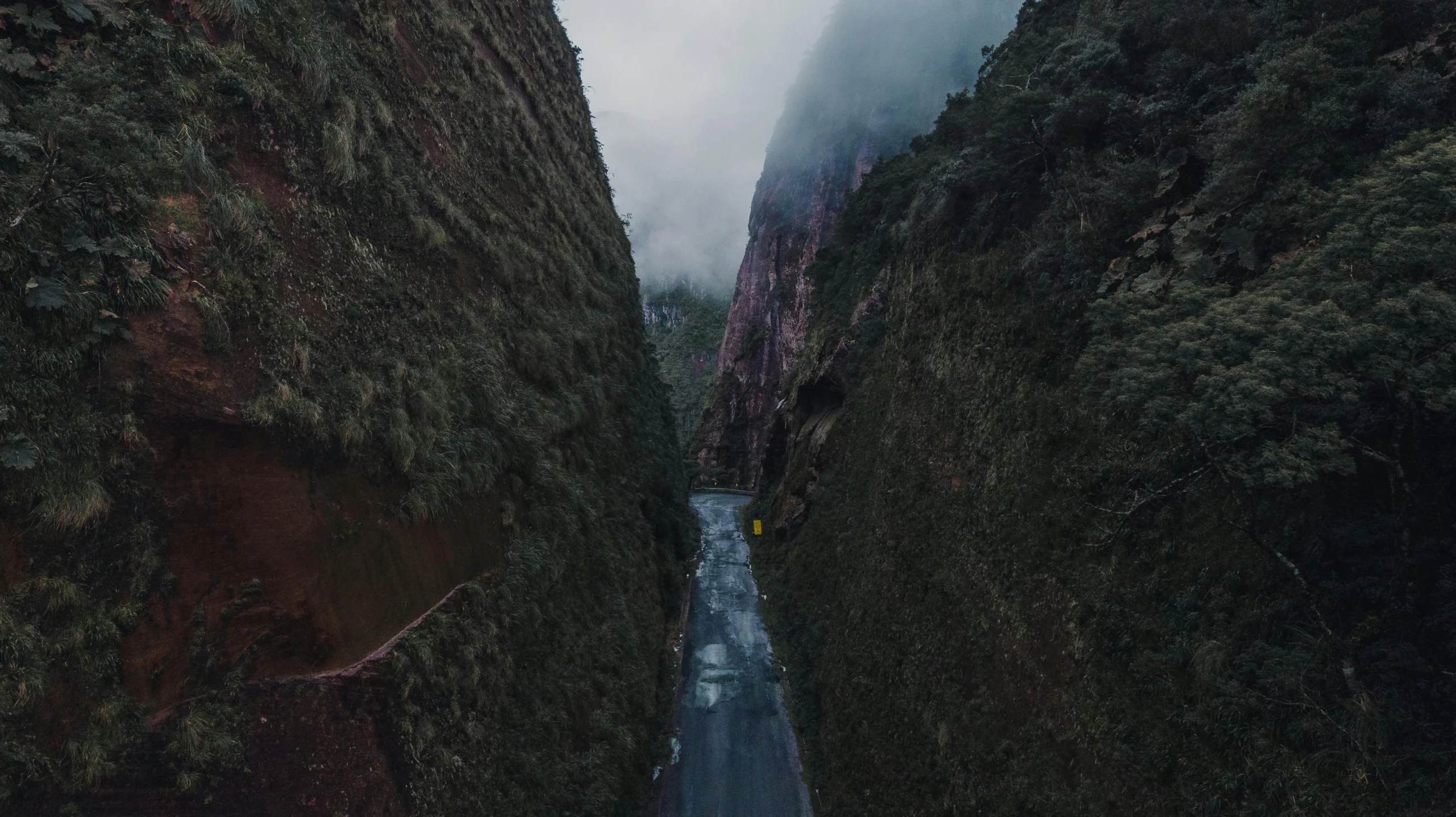 a narrow road with two roads between two huge mountains