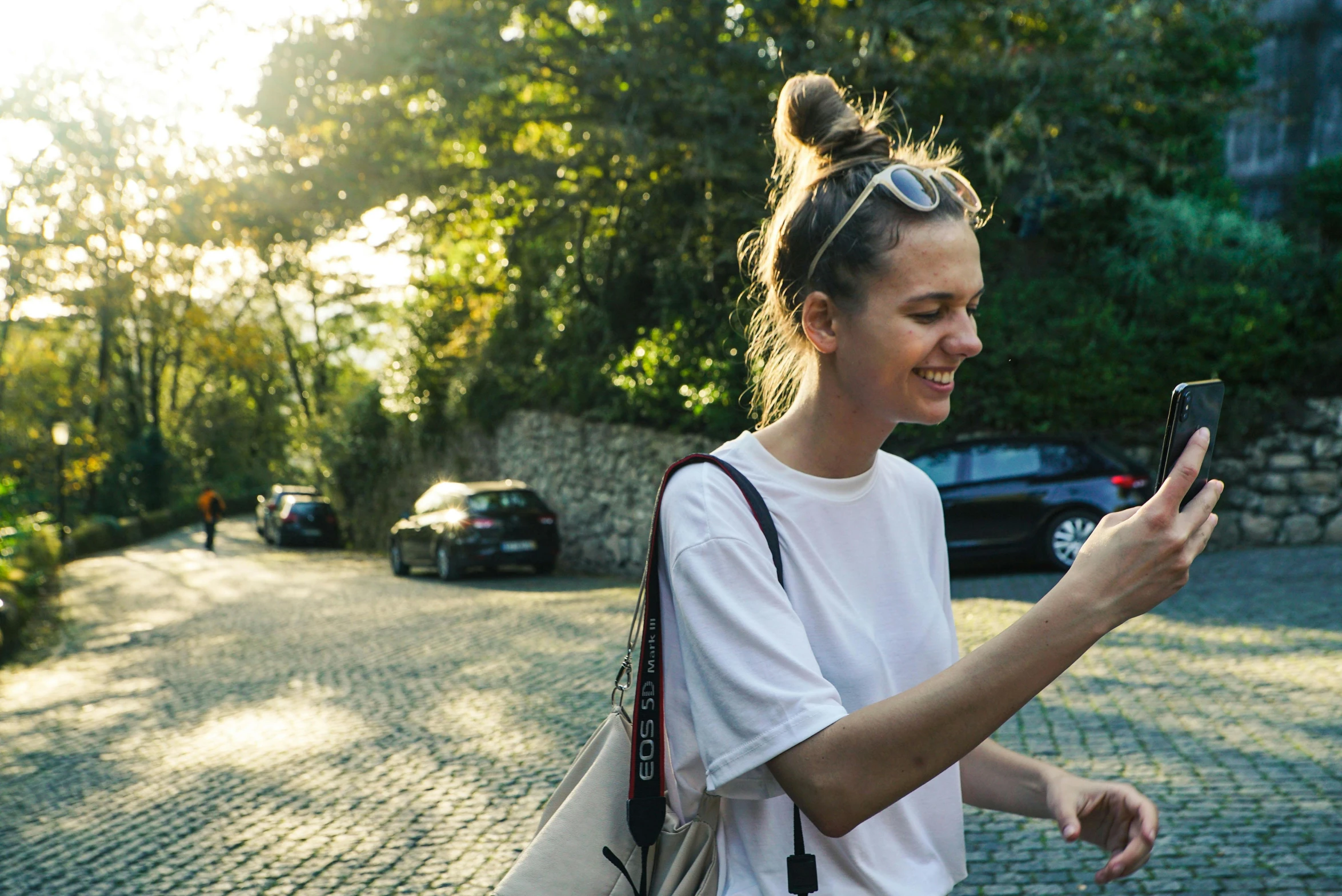 woman wearing white is walking down the street using a cellphone