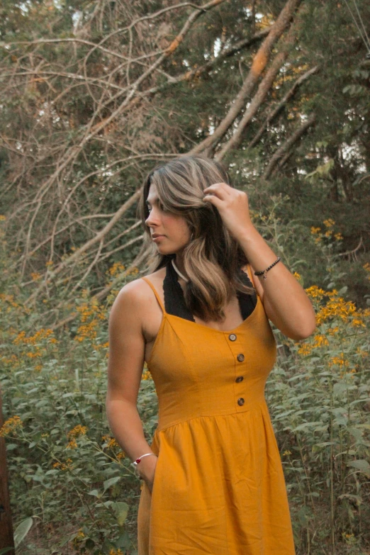 a woman in a yellow dress stands by some trees