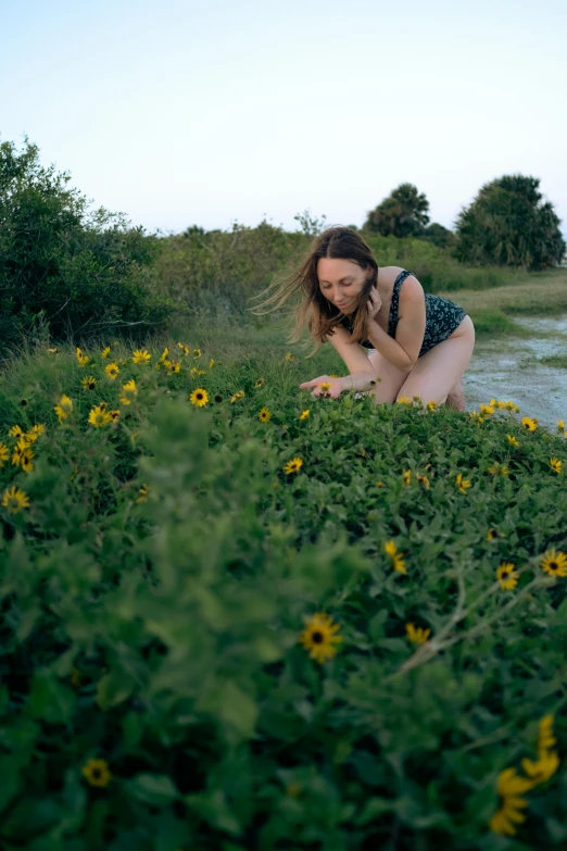 a woman in a bathing suit crouches down in the grass