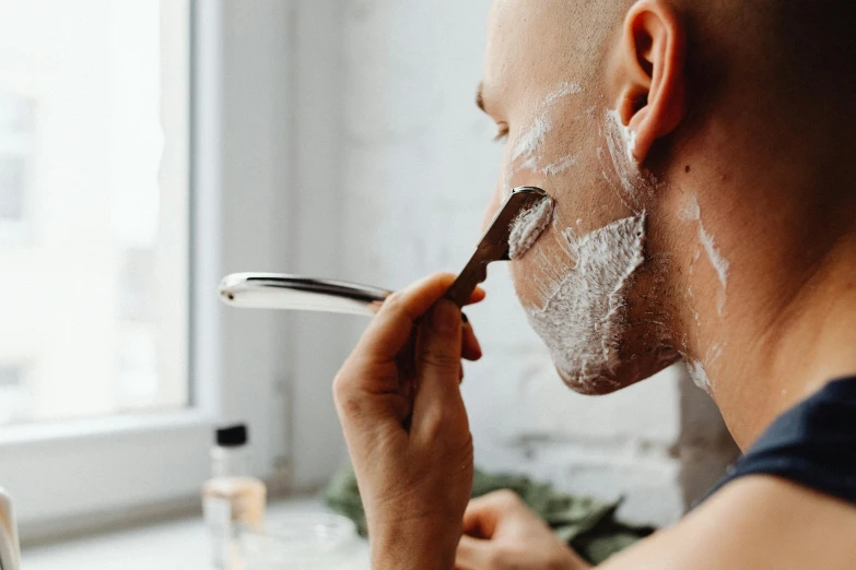 man shaving with facial mask on face while looking out a window