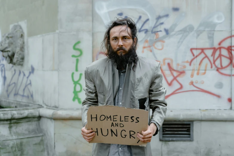 a man standing with a sign that reads homeless and hungry