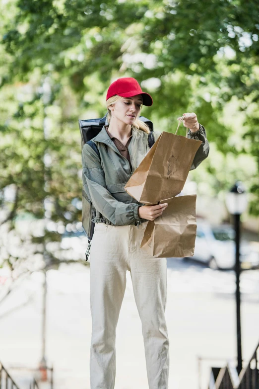 a woman in a red cap and white pants holding a brown bag