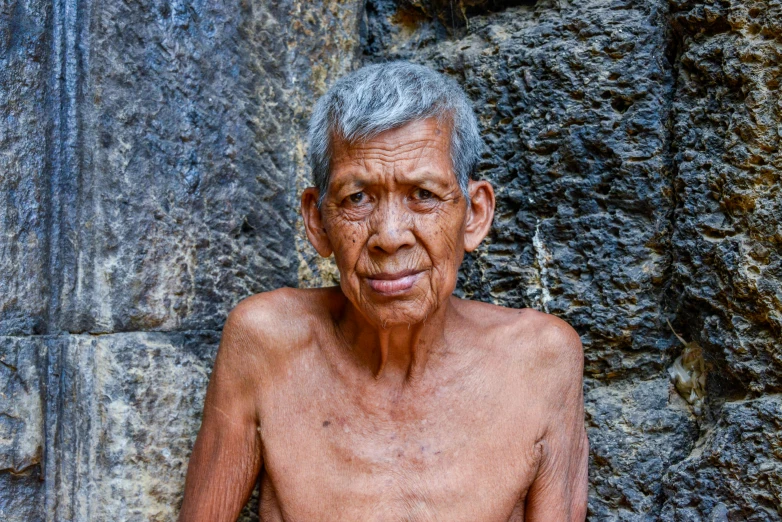 an older man standing in front of a stone wall