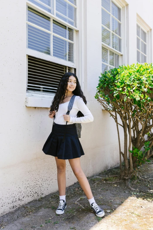 a girl in a white top and black skirt posing by a window