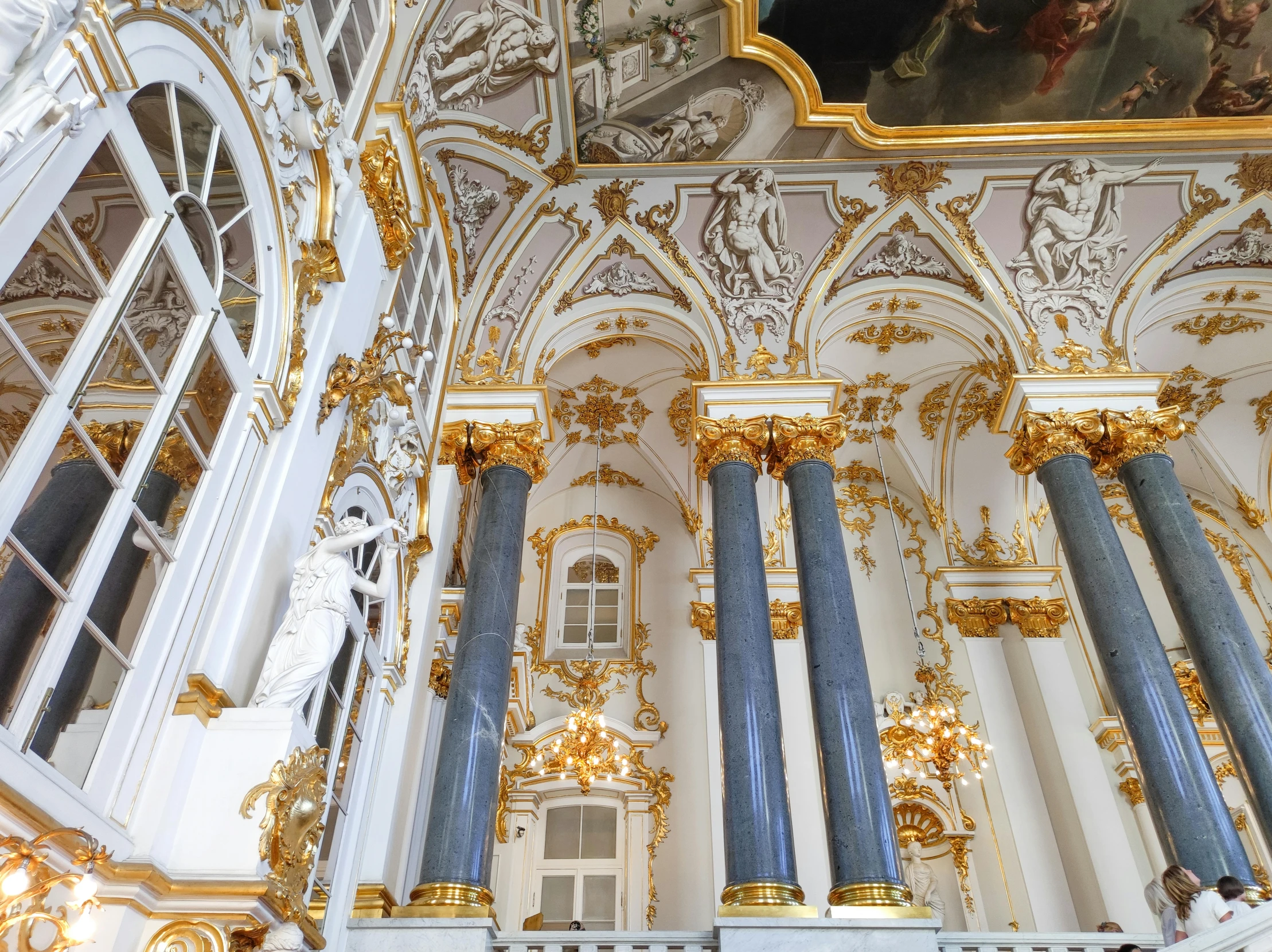 a po from inside of the white palace, looking up at a large painted ceiling and golden pillars