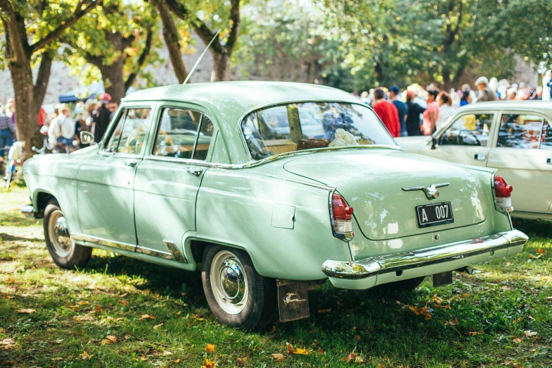 two old cars in the grass and people looking around