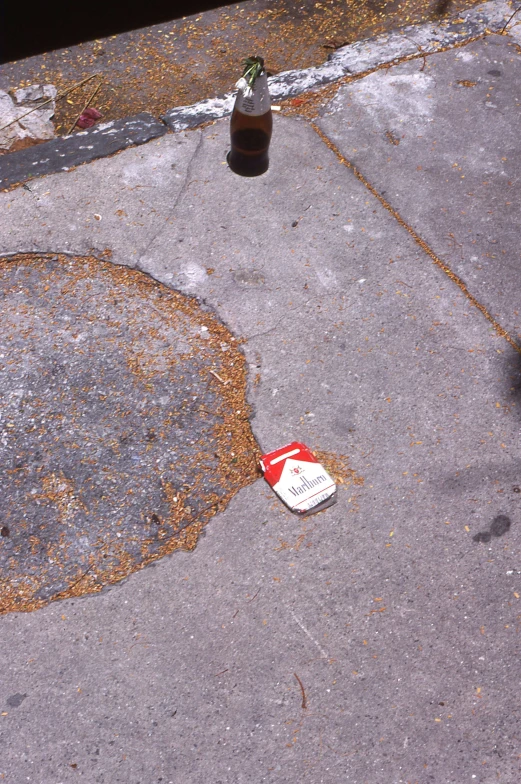 a beer bottle sitting on the curb near a patch of asphalt