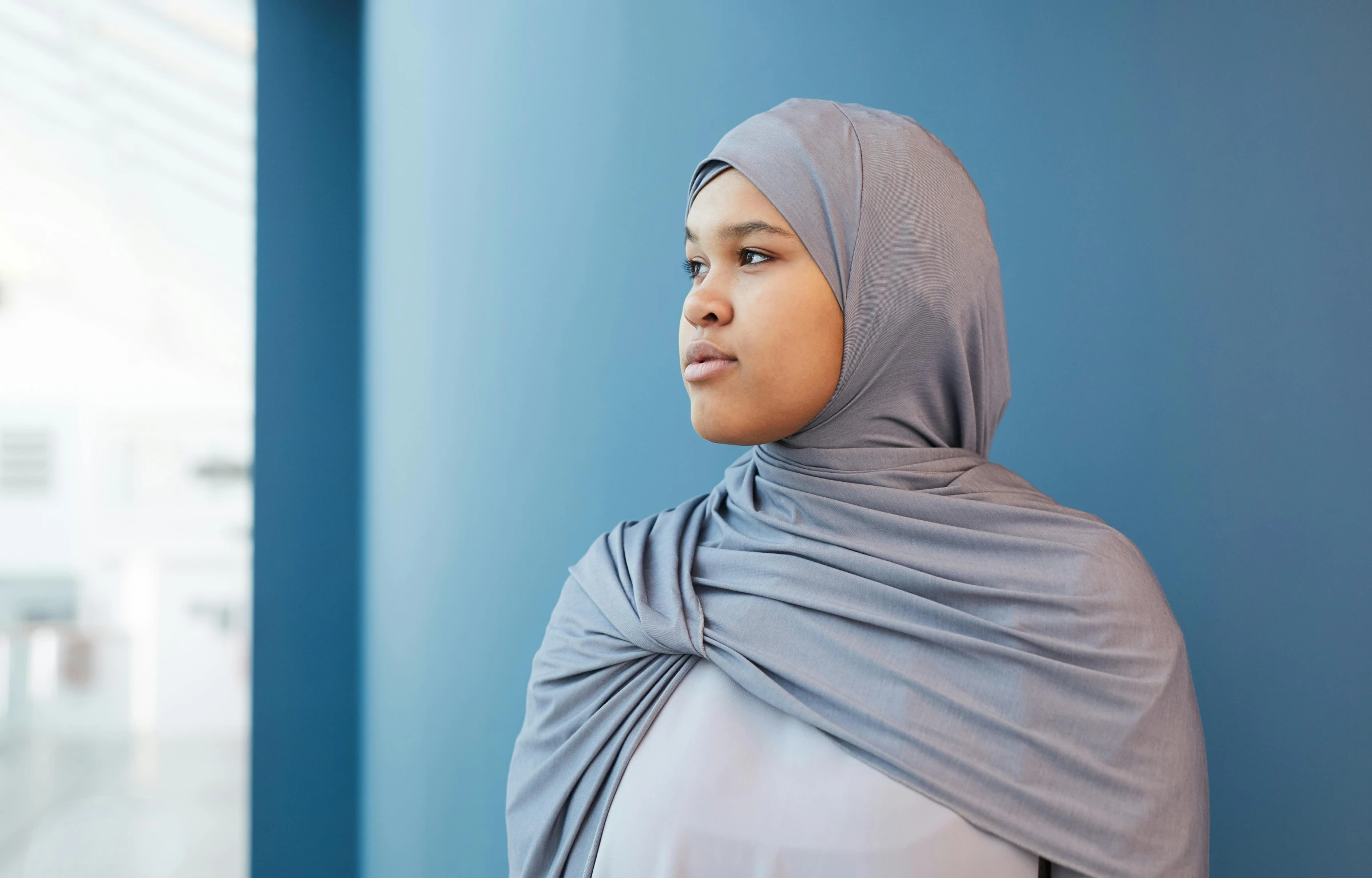 a woman wearing a blue scarf standing by a wall