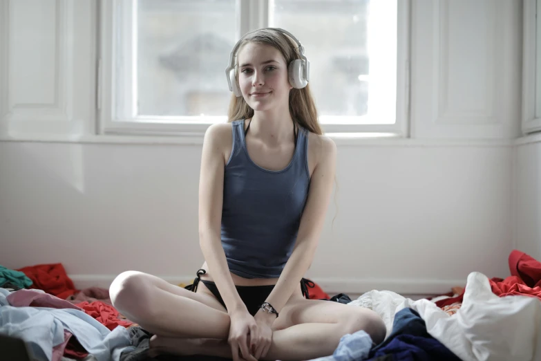 girl in headphones sitting on messy bed