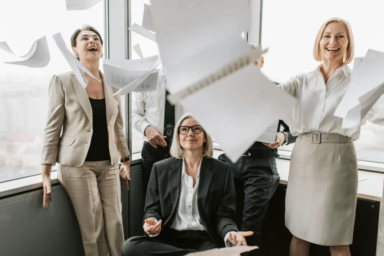 three women in business suits laugh and laugh while holding papers