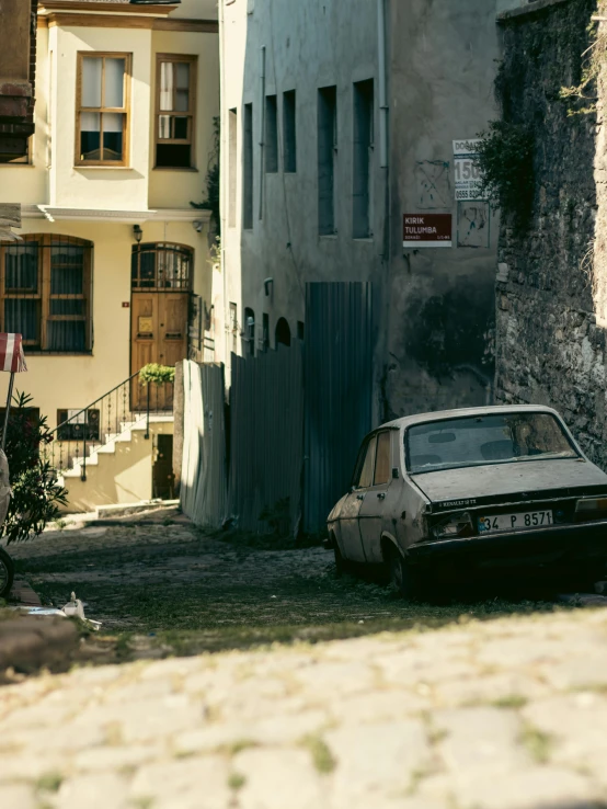 an old run down car is parked on the side of a stone path in a small urban neighborhood