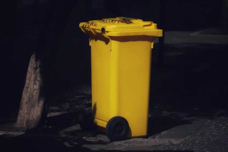 a yellow trash can sitting in front of a tree