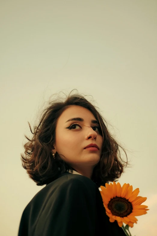 a young woman with dark hair and sunflower in her hand