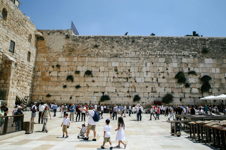 a large group of people are walking around in front of a big stone wall