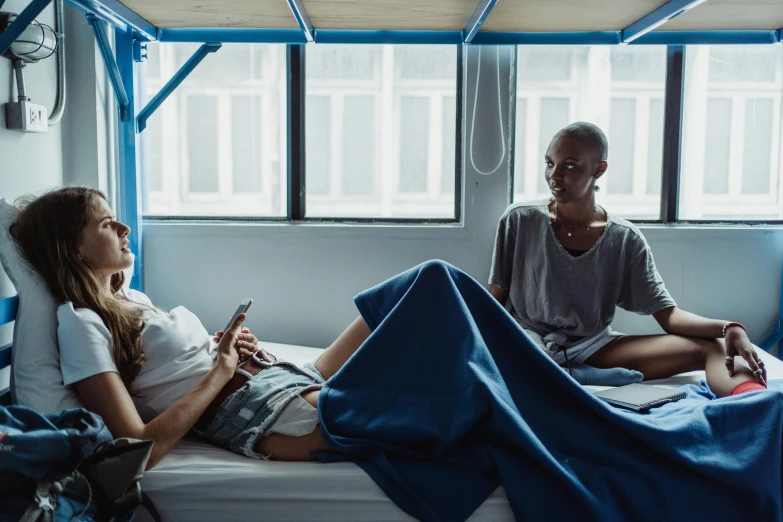 two people sitting on top of a bed next to each other