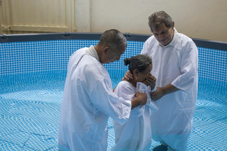 three men are around a small child who is wrapped in white fabric