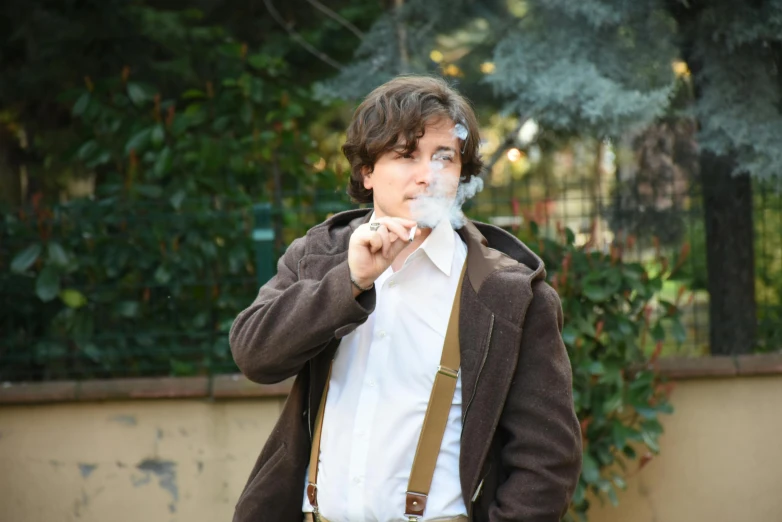 a young man smokes a cigarette while dressed in a jacket