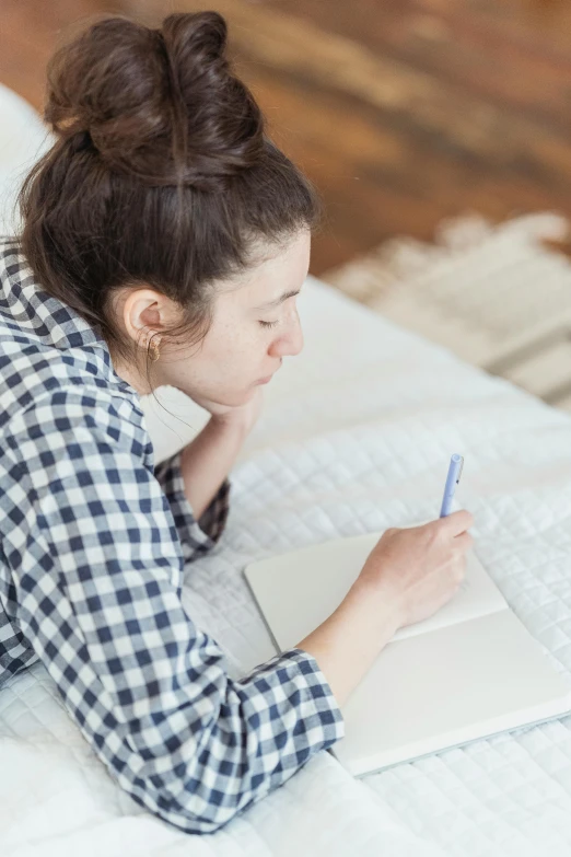 woman writing on a notebook on a bed