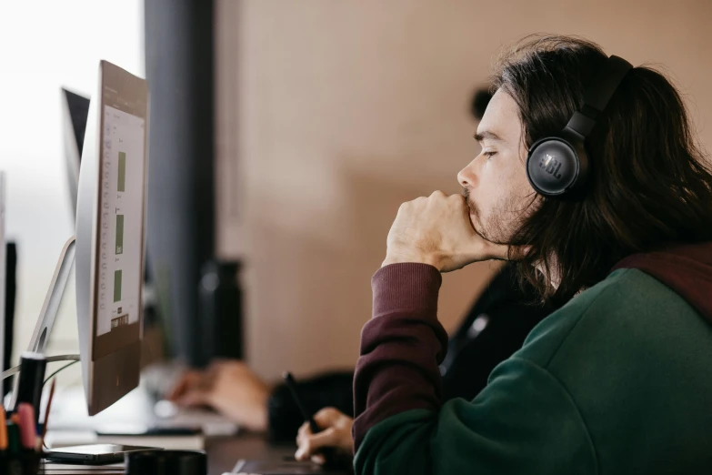 a person sitting at a desk with headphones on and looking at a computer monitor