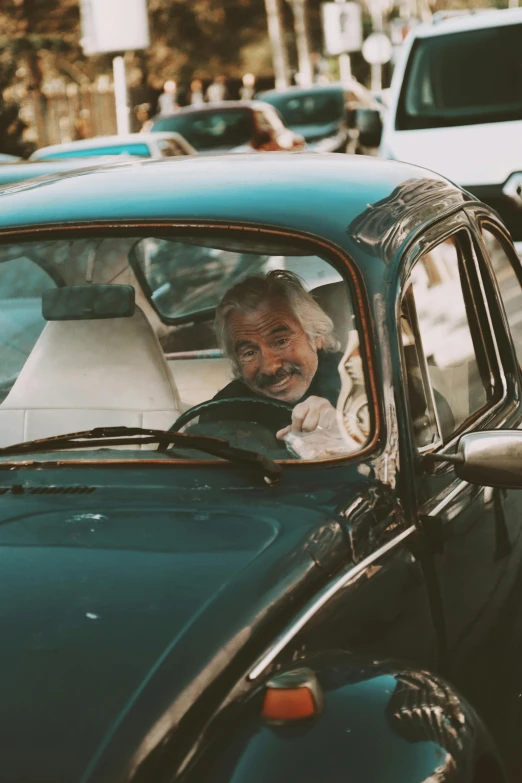 older man smiling in old car parked on the side walk