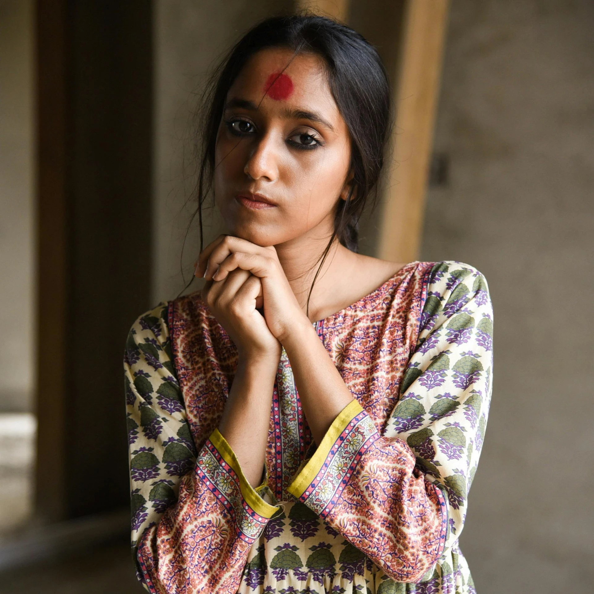 a woman with her hand on her chin standing in front of a wall