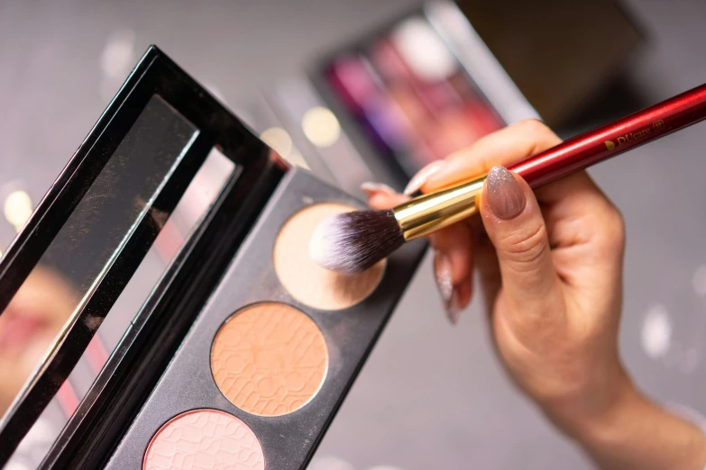a woman holding makeup brushes, next to some makeup