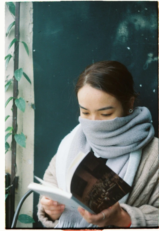 a woman reads a book while wearing a scarf