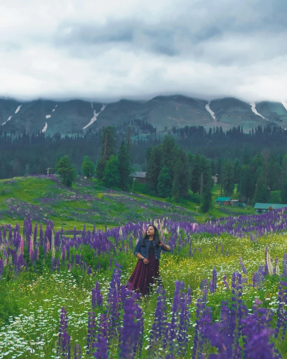 a woman in purple and green is walking in a field of flowers