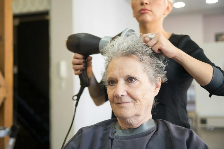 an older lady at the hair salon blow drying her hair