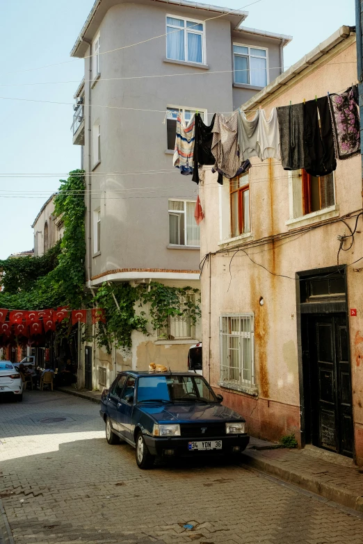 a blue car parked next to a building with washing hanging over the doorways