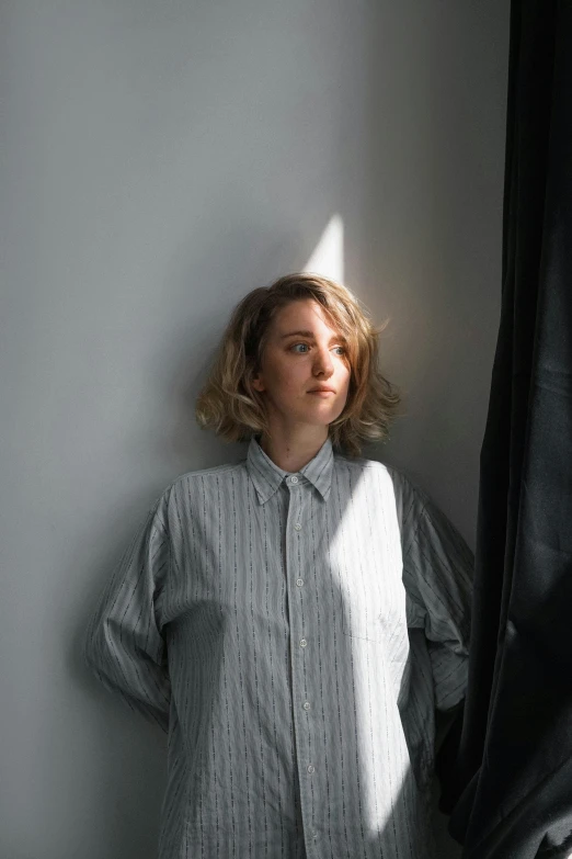 a young woman leans against a wall in a on - down shirt