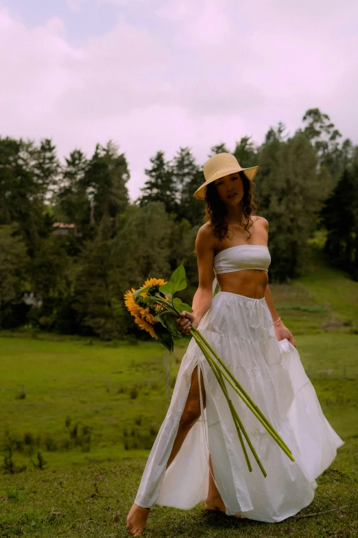 woman in white dress holding yellow flowers and a straw hat