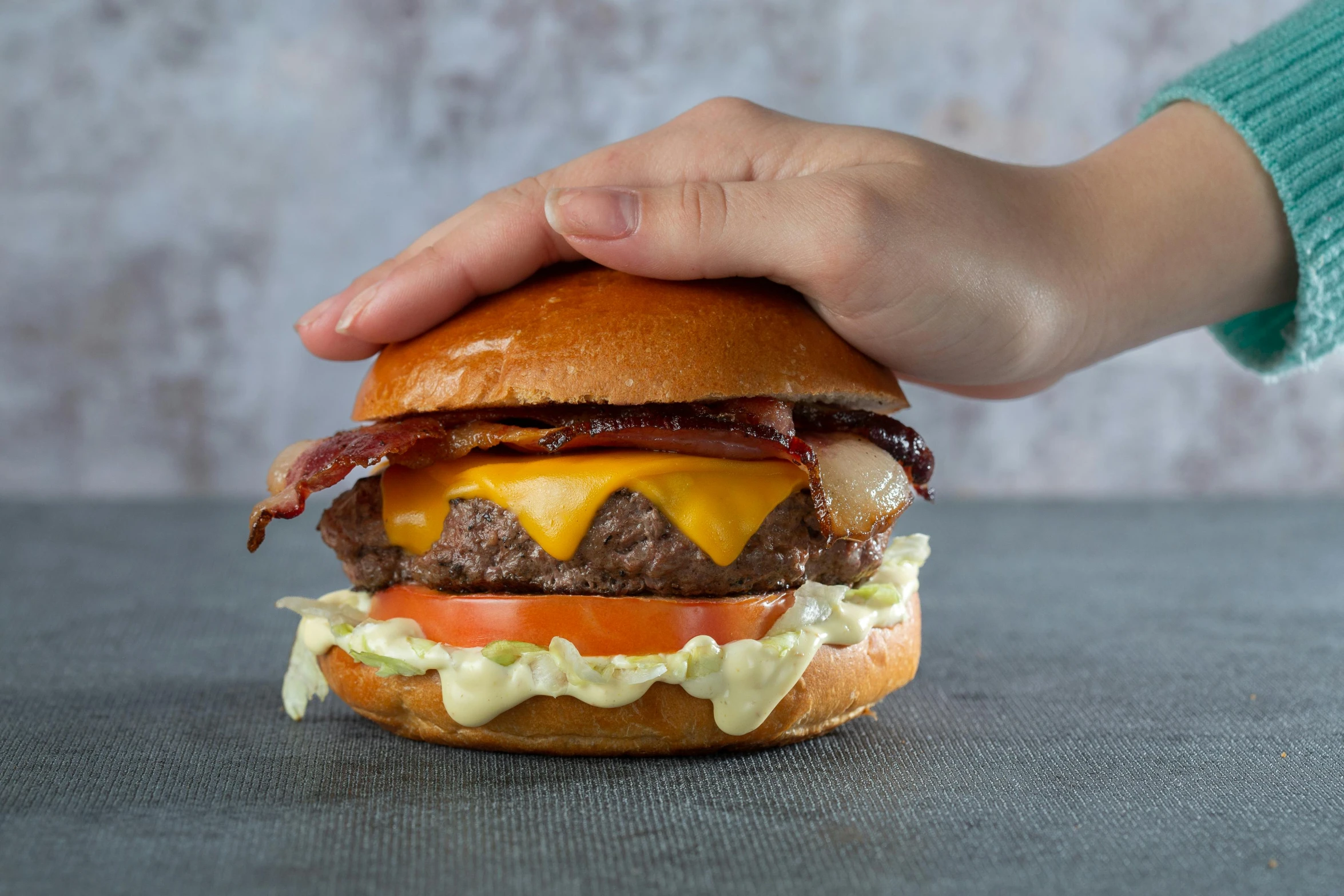 a hand holding a cheeseburger over a table