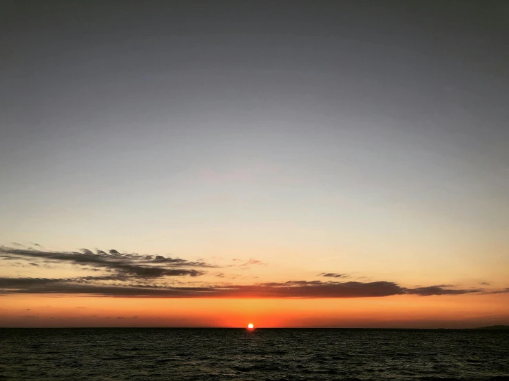 a lone kite flying above the ocean as the sun sets