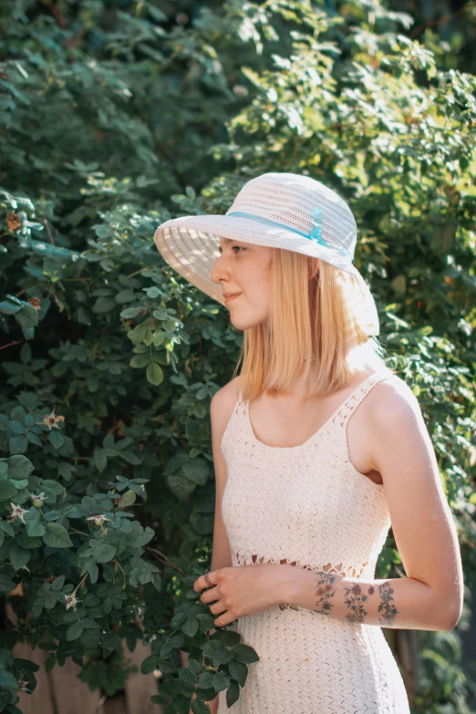 a pretty blonde wearing a white hat by a tree