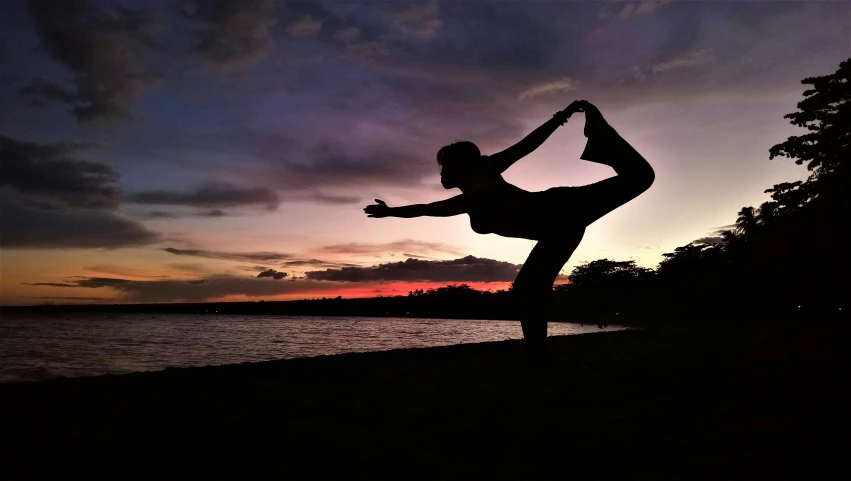 the person is doing yoga at sunset by the water