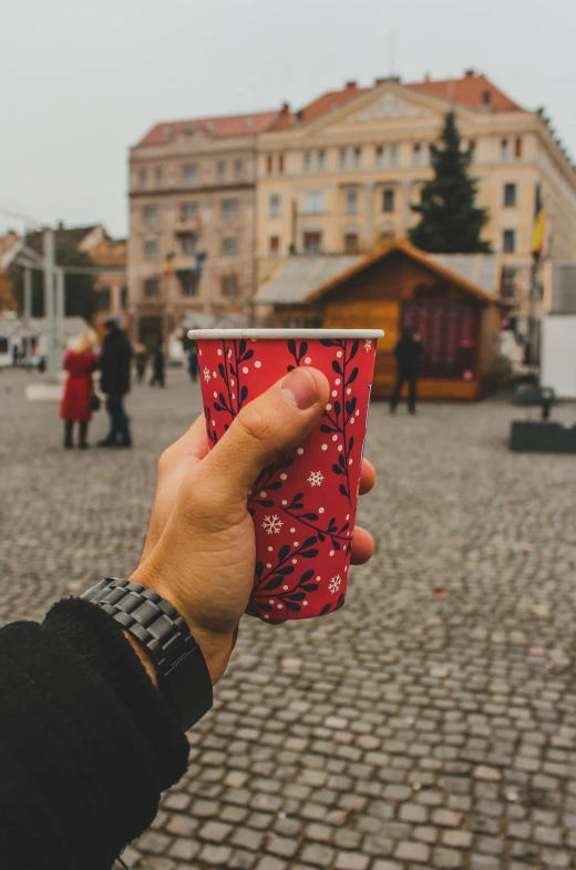 a hand holding a small red cup on a brick walkway