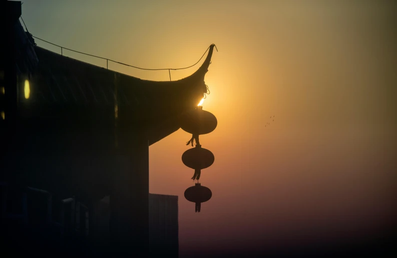 the sun is setting over a building with a wind chime