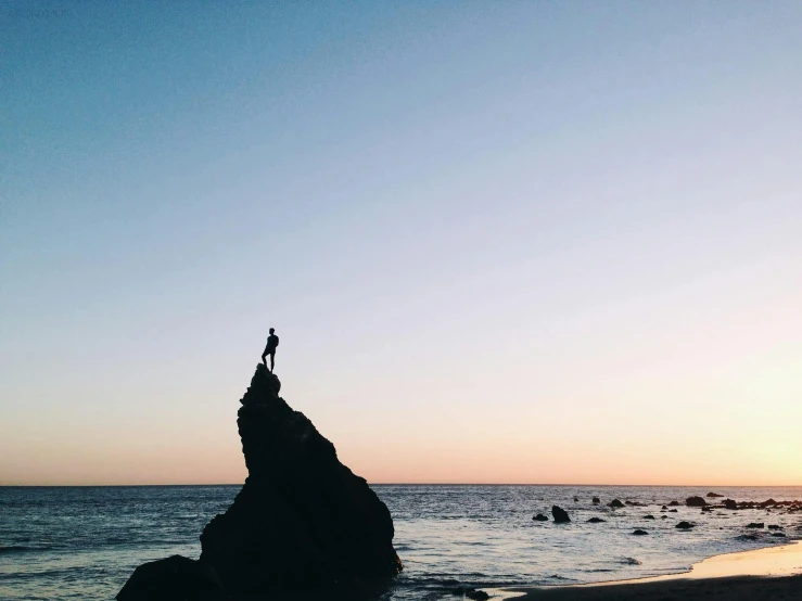 the person on top of the rock stands at the edge of the water