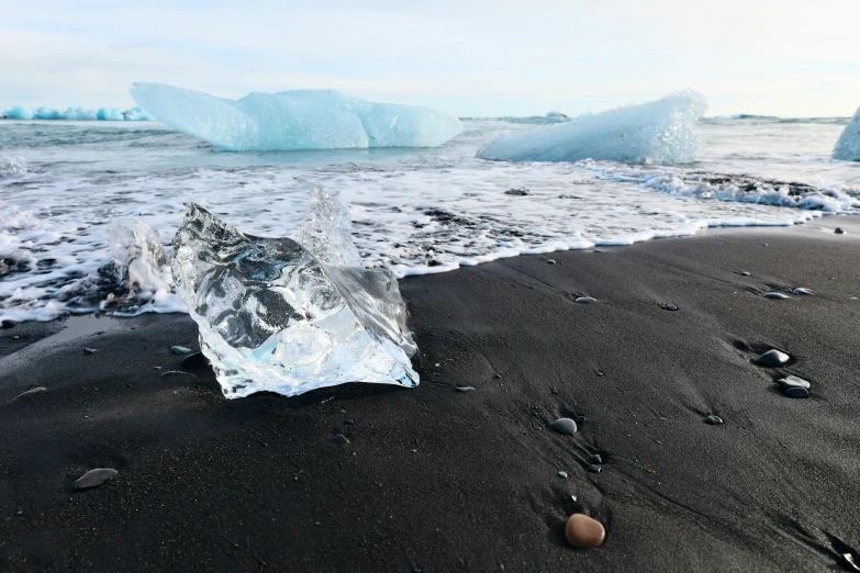 a glass bottle lies on the beach near some icebergs