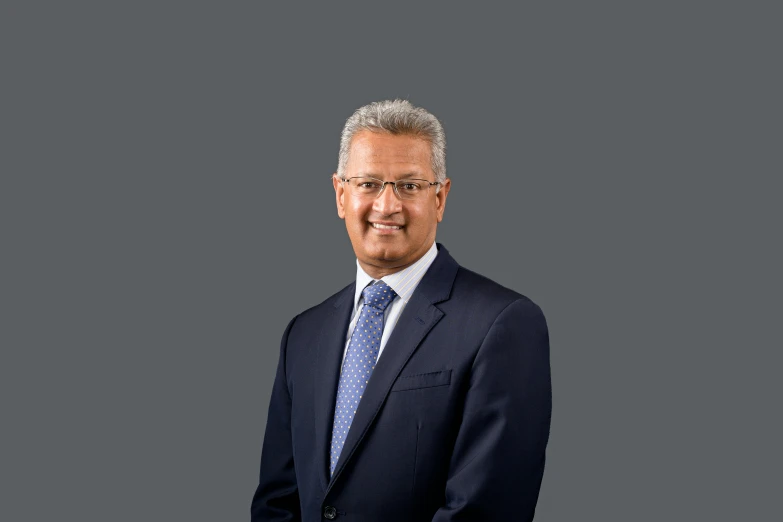 a man wearing glasses, standing in front of a gray background