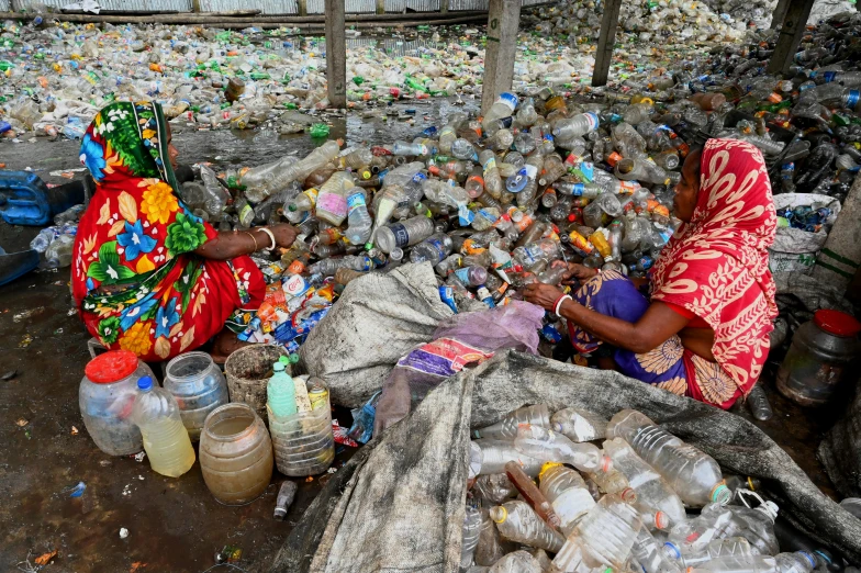 the women are sitting near several bags of garbage