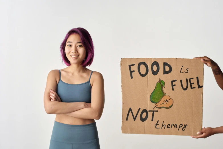 a woman standing with her arms crossed holding a sign with the words food is not fuel, the other sign says therapy