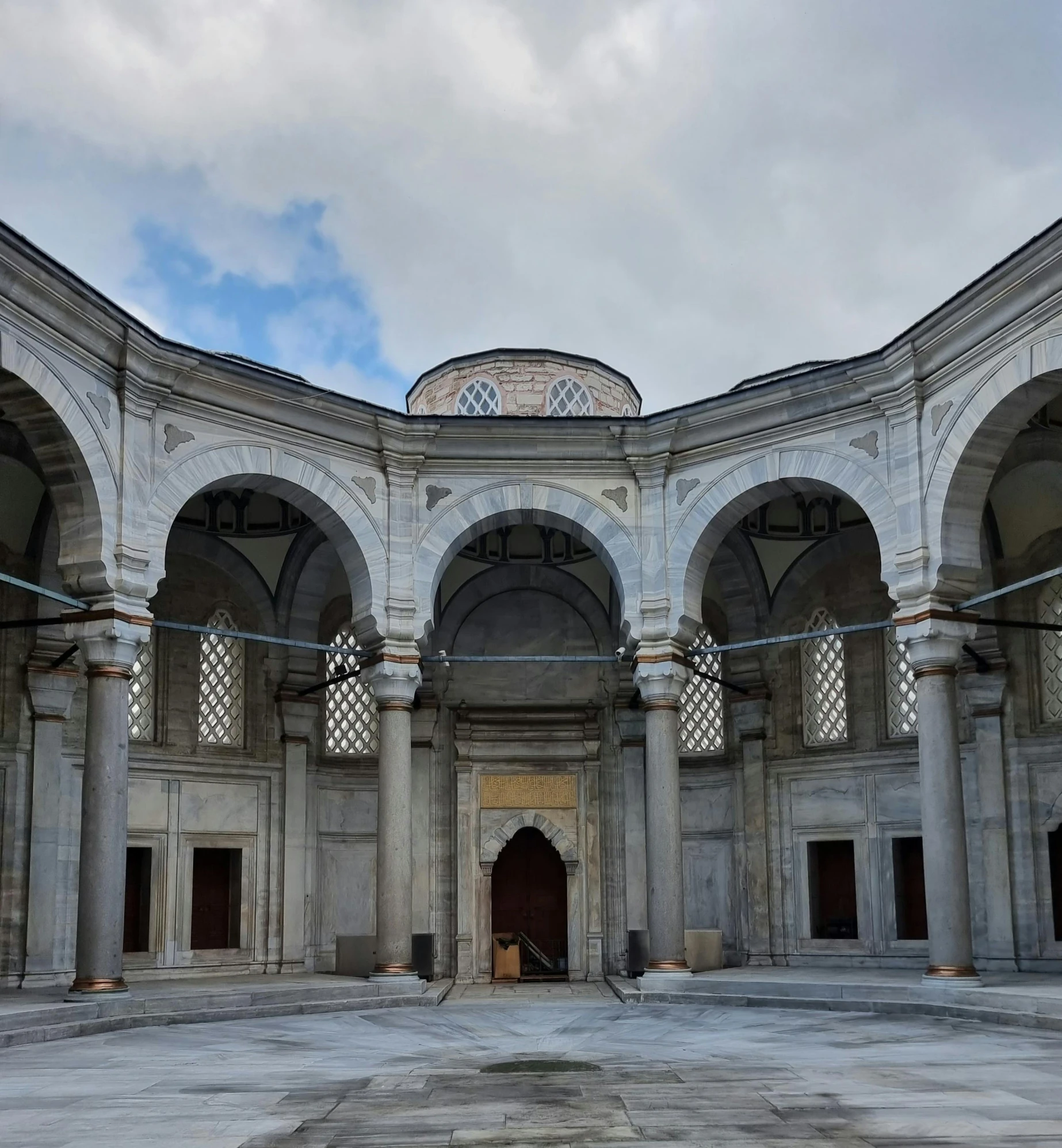 a courtyard full of stone columns and doors with cloudy skies in the background