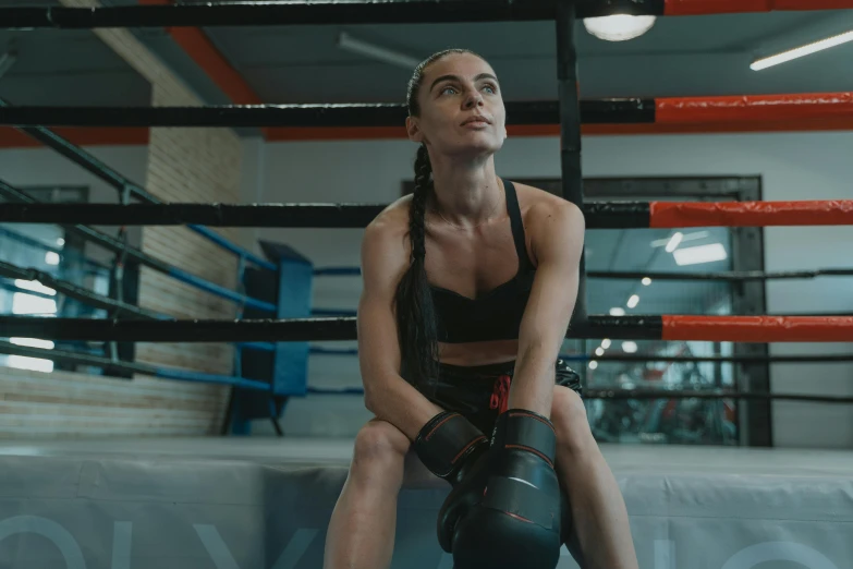 a woman sitting on the edge of a boxing ring with a punching bag in her hand