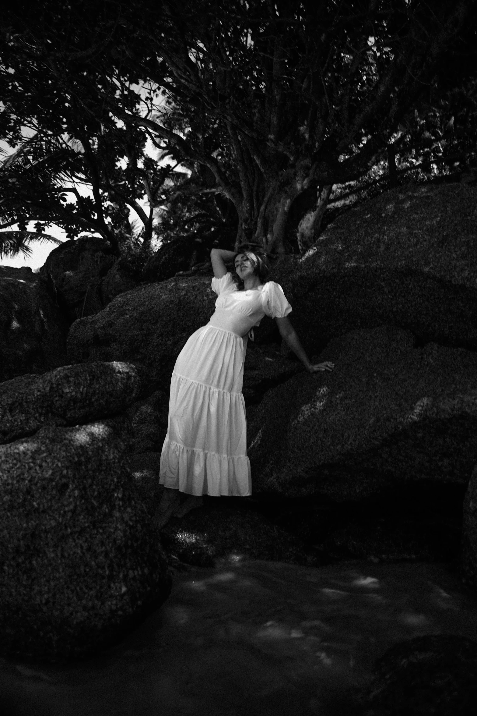 a woman is standing by some rocks near a tree