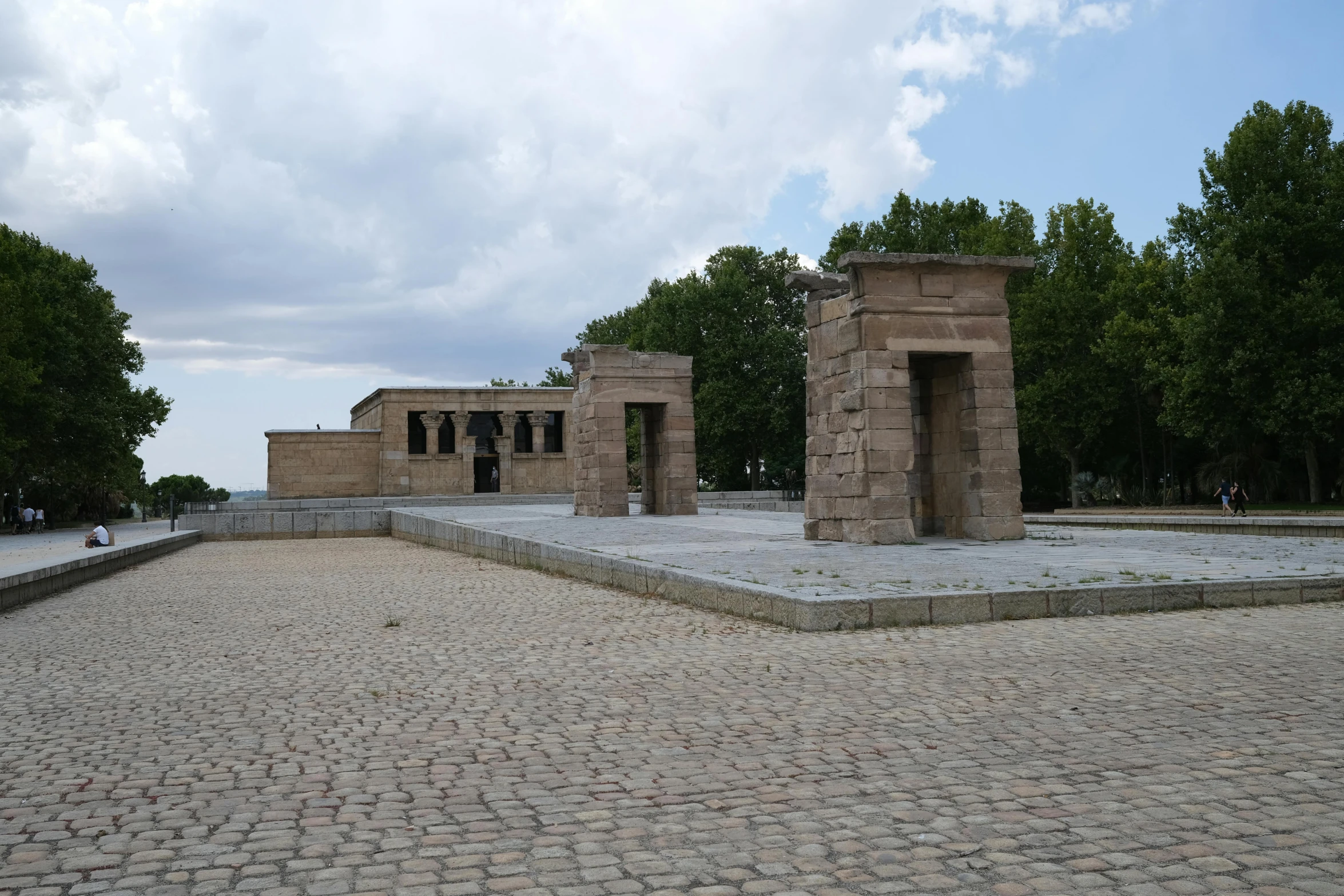 a stone structure in front of trees on cobblestone ground