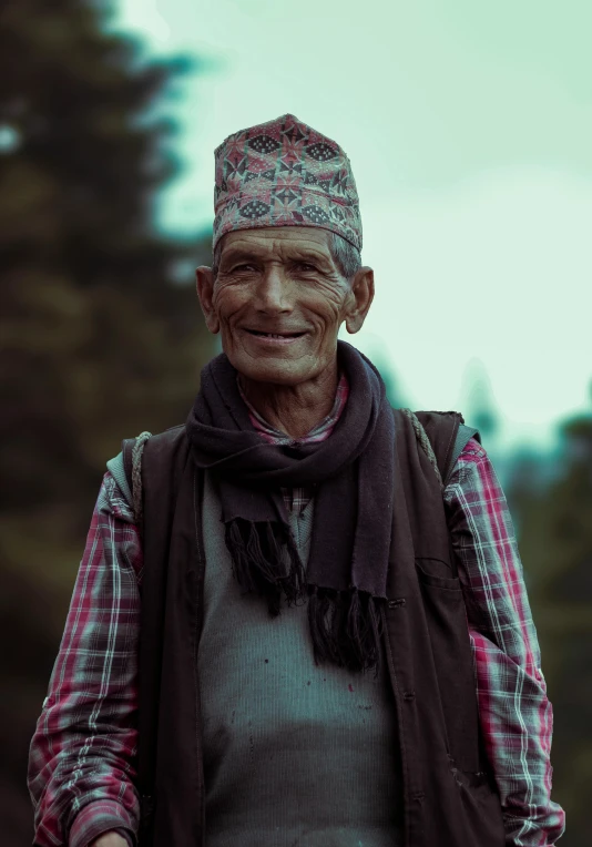 a man wearing a hat and scarf stands in front of trees